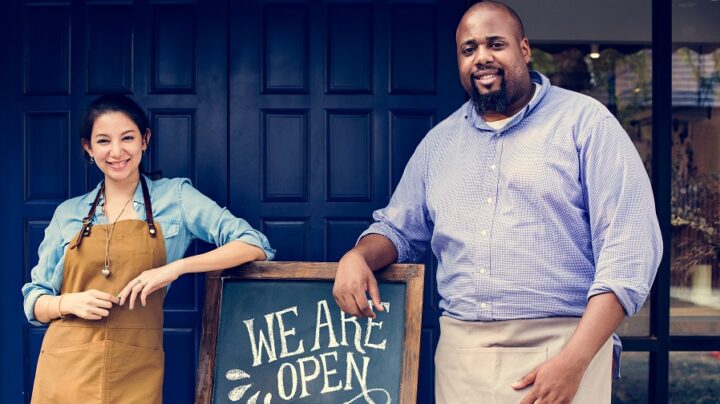 Cheerful business owners standing with open blackboard