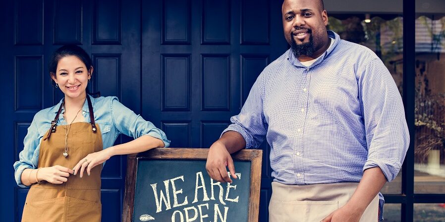 Cheerful business owners standing with open blackboard