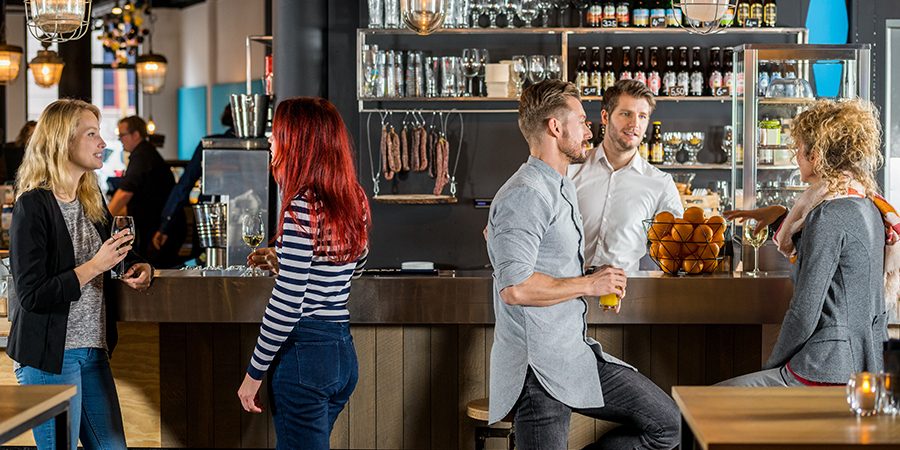 Friends Talking While Having Their Drinks In Bar Young friends talking while having their drinks at bar counter