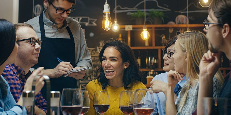 In the Bar/ Restaurant Waiter Takes Order From a Diverse Group o In the Bar/ Restaurant Waiter Takes Order From a Diverse Group of Friends. Beautiful People Drink Wine and Have Good Time in this Stylish Place.