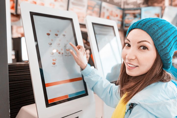 A woman orders food in the touch screen terminal with electronic menu in fast food restaurant