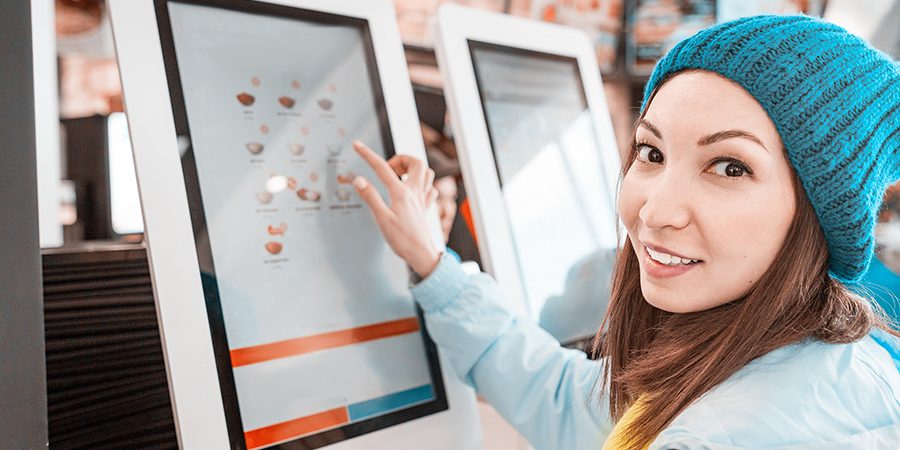 Happy Asian woman orders food in the touch screen terminal with electronic menu in fastfood restaurant. Modern technology concept A woman orders food in the touch screen terminal with electronic menu in fast food restaurant